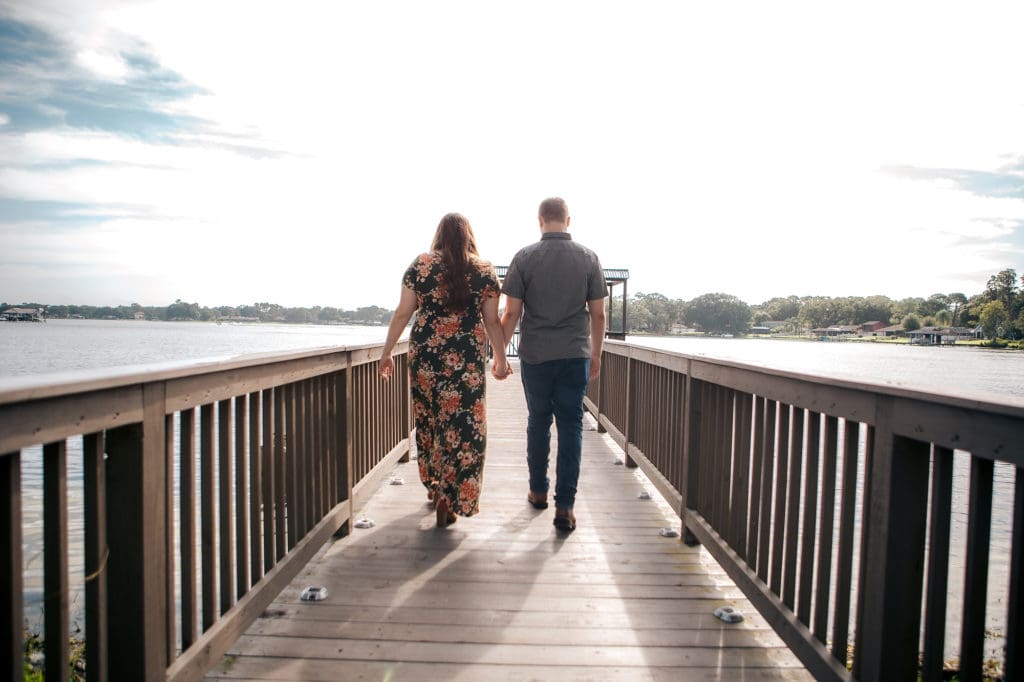 Engaged couple holding hands on dock at Knotted Roots on the Lake