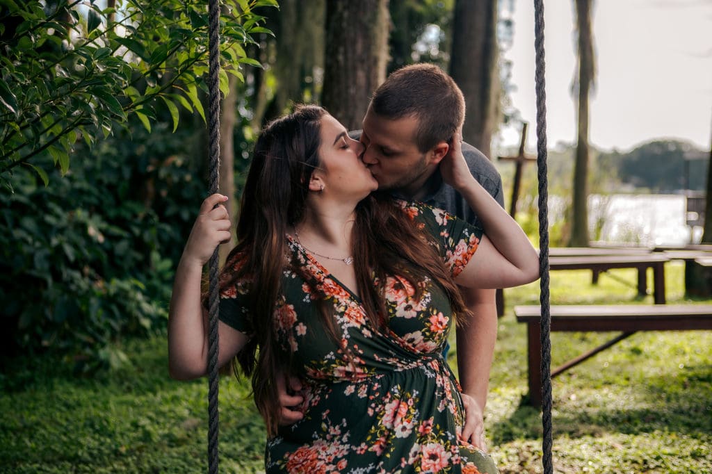 Engaged couple kissing on swing at Knotted Roots on the Lake